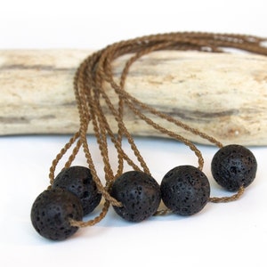 Pode incluir: Um conjunto de seis contas de pedra de lava preta enfiadas em cordões marrons. As contas são redondas e têm uma superfície áspera e texturizada.