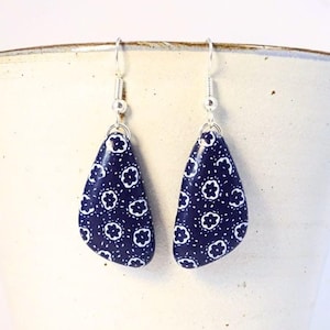 Könnte beinhalten: Ein Paar marineblaue Tropfenohrringe mit weißem Blumenmuster. Die Ohrringe hängen an silberfarbenen Fischhaken-Ohrdrähten. Die Ohrringe werden vor einem weißen Hintergrund präsentiert.