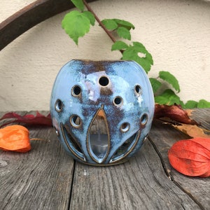 May include: A blue ceramic candle holder with a decorative design and cut-out details. The holder is round and has a rustic, glazed finish.