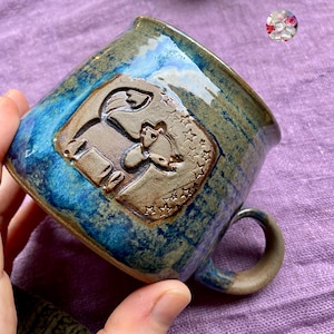 May include: Handmade ceramic mug with a blue and brown glaze. The mug features a raised relief design of a horse and stars. The handle is a matching brown colour. A unique piece for coffee or tea.