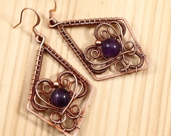 May include: A pair of copper wire earrings with amethyst gemstones. The earrings are in the shape of a diamond with intricate wire designs.