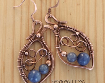 May include: Copper wire-wrapped earrings with blue gemstone beads. The earrings have a teardrop shape with intricate wire detailing and a hook closure. The text "TOTALLY wired by Maria" is visible in the bottom right corner.