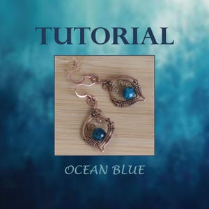 May include: A pair of copper wire earrings with a teardrop shape and a blue gemstone in the center. The earrings are on a wooden surface. The text "Ocean Blue" is below the earrings.