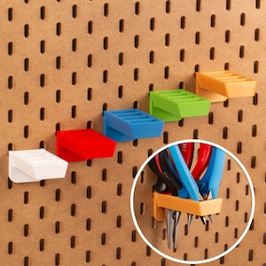 Puede incluir: Cinco organizadores de pared de plástico de colores con ranuras para guardar objetos pequeños, montados en una pared de tablero de clavijas. Un organizador contiene un juego de alicates y cortadores de alambre.
