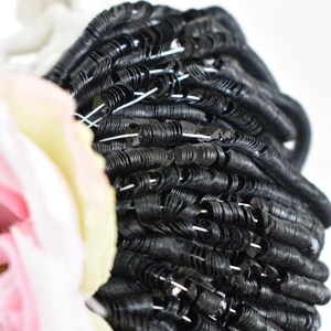 May include: A close-up of a large spool of black sequins. The sequins are arranged in a spiral pattern and are shiny and reflective.
