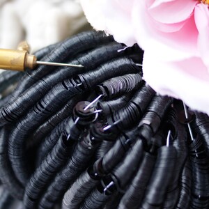 May include: A close-up of black sequins, arranged in a circular pattern, with a needle and thread tool visible in the center.