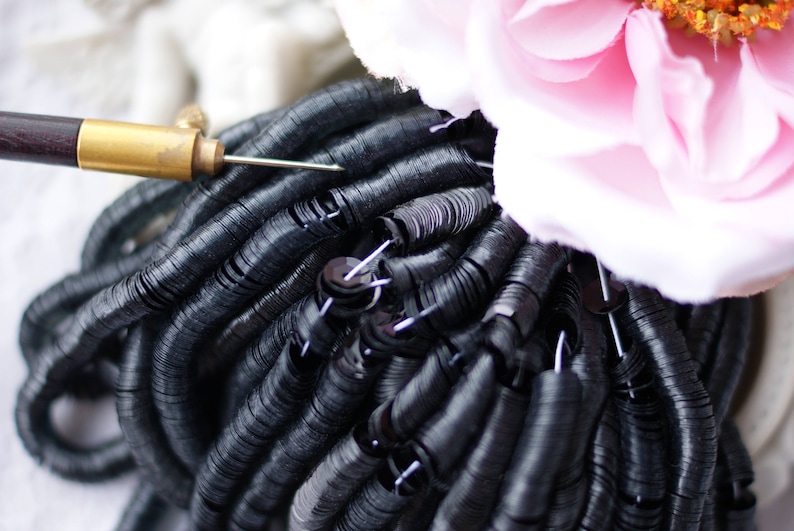 May include: A close-up of black sequins, arranged in a circular pattern, with a needle and thread tool visible in the center.