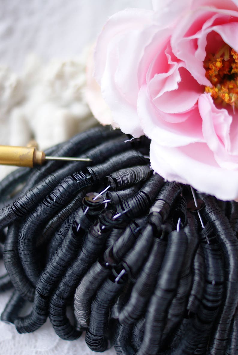 May include: A close-up of a large pile of black sequins. The sequins are arranged in a circular pattern, creating a swirling effect.