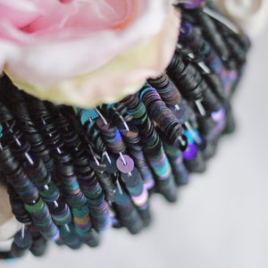 Pode incluir: Close-up de uma flor de tecido rosa com lantejoulas pretas iridescentes costuradas ao redor da base.