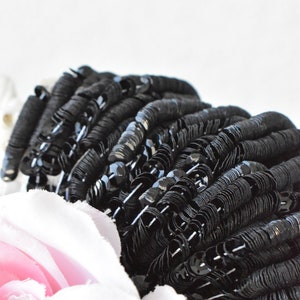 May include: Black sequins in a pile, arranged in a circular pattern. The sequins are shiny and have a slight metallic sheen.