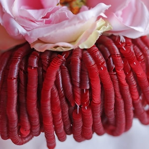 May include: A close-up of a pile of red sequins. The sequins are arranged in a circular pattern, creating a textured and shimmering effect.