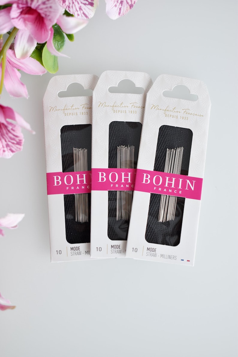 May include: Three packages of Bohin straw millinery needles. Each package is white with black text and a pink stripe. The text on the packages reads "Manufacture Fran&ccedil;aise Depuis 1833" and "Bohin France".