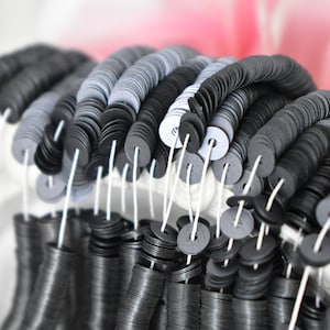 Pode incluir: Close-up de uma grande quantidade de lantejoulas pretas e prateadas enfiadas em um fio branco. As lantejoulas estão dispostas em filas e penduradas em uma superfície branca.