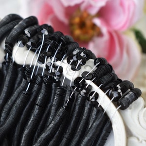May include: Black sequins and black metallic beads strung on white thread. The beads are arranged in a circle, with the sequins in the center.