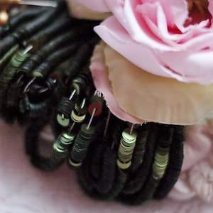 May include: Close-up of a black and green sequined trim with a pink rose and white fabric in the background.