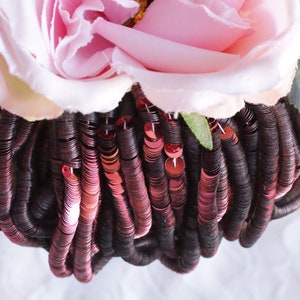 Pode incluir: Um close-up de um monte de lantejoulas bordô com uma flor de tecido rosa no topo.