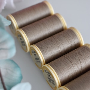 Può includere: Sei bobine di filo marrone chiaro con etichette color crema. Le etichette hanno testo nero che recita "Fil Au Chinois 30/2 100% Cotone Made in France".