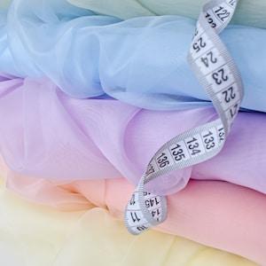 May include: A stack of pastel colored sheer fabric with a white measuring tape on top. The tape reads 10, 11, 12, 13, 14, 15, 16, 17, 18, 19, 20, 21, 22, 23, 24, 25, 32, 33, 34.