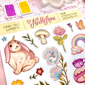 May include: A sheet of stickers featuring a whimsical fairy tale garden theme. The stickers include a unicorn rabbit, mushrooms, flowers, a rainbow, and a teacup.