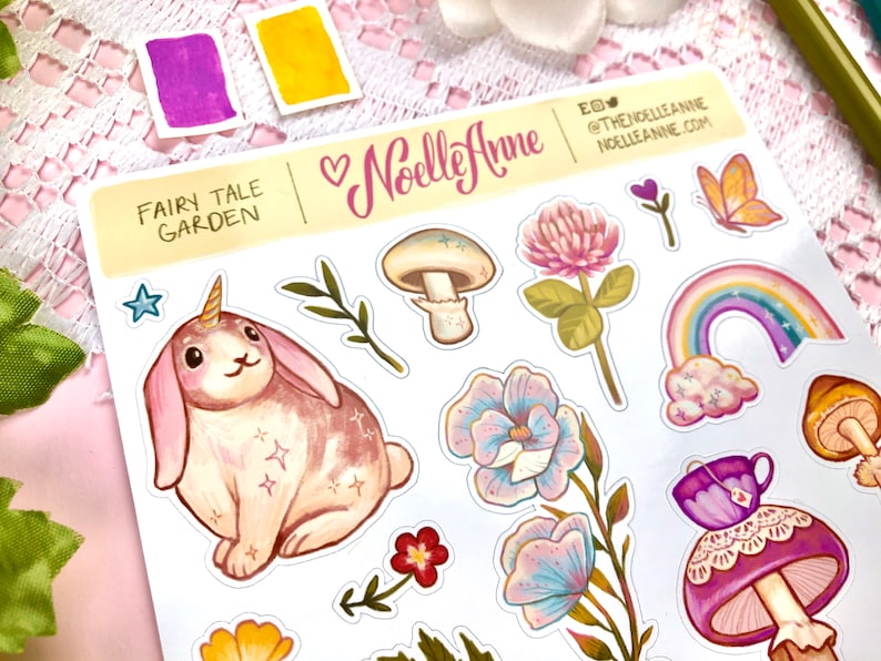 May include: A sheet of stickers featuring a whimsical fairy tale garden theme. The stickers include a unicorn rabbit, mushrooms, flowers, a rainbow, and a teacup.
