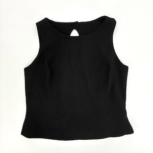 May include: A solid black sleeveless top featuring a high rounded neckline and a small teardrop-shaped cutout detail at the upper center. The garment has a clean, structured silhouette with a straight hemline, providing a simple and versatile look.