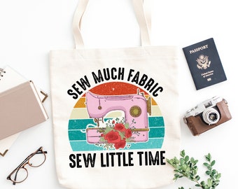 May include: A white canvas tote bag with a vintage-style graphic of a sewing machine and flowers. The text on the bag reads "Sew Much Fabric Sew Little Time".