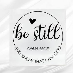 May include: A square, white sign with black text. The words "be still" are in a cursive font, inside a black circle with a black heart at the top. The text "AND KNOW THAT I AM GOD" is in a circular font around the bottom. The text "PSALM 46:10" is in the center.