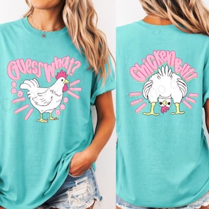 May include: Teal t-shirt with a playful chicken graphic. The front features a white chicken with the text "Guess What?" in pink. The back displays a chicken's rear with the text "Chicken Butt" in pink. A fun and quirky design.