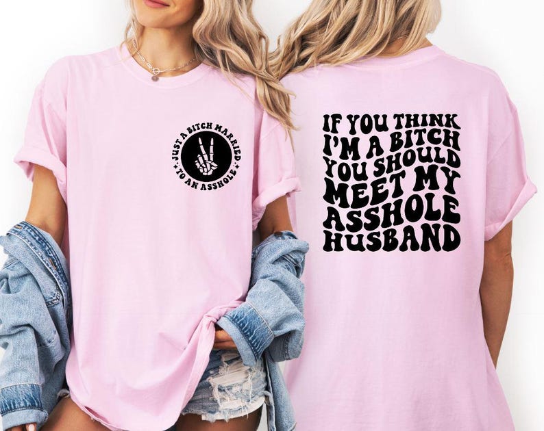 May include: A light pink t-shirt with the text "JUST A BITCH MARRIED TO AN ASSHOLE" on the front and "IF YOU THINK I'M A BITCH YOU SHOULD MEET MY ASSHOLE HUSBAND" on the back. The front graphic is a circle with a peace sign made of a skeleton hand.