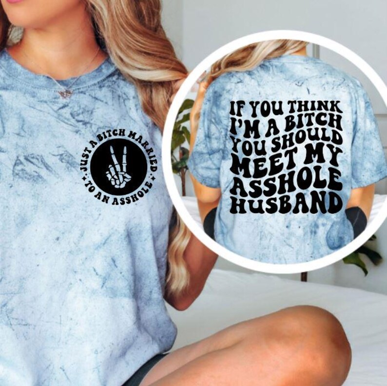 May include: A light blue tie-dye t-shirt with the text "Just a Bitch Married to an Asshole" on the front and "If you think I'm a bitch you should meet my asshole husband" on the back. The shirt features a peace sign made of bones.