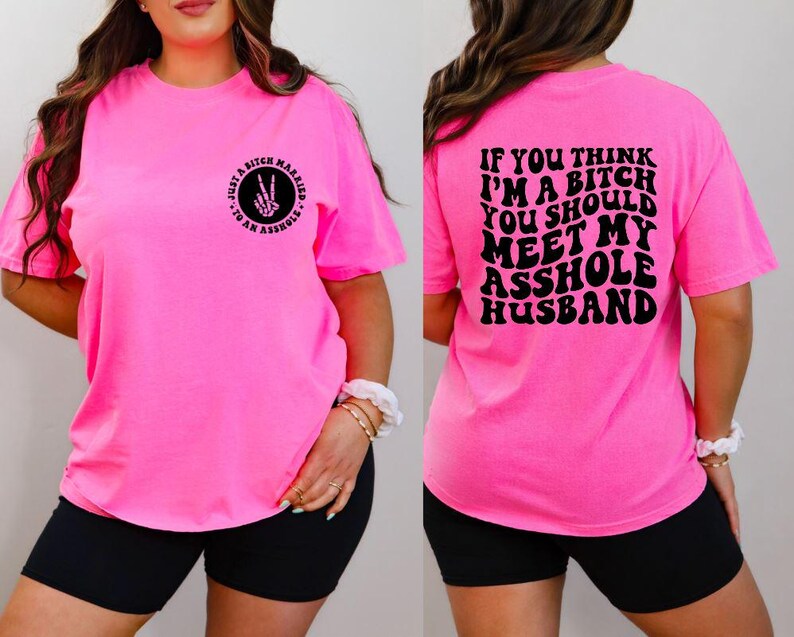 May include: Bright pink t-shirt with black text on the front and back. The front reads "Just a bitch married to an asshole" with a peace sign made of bones. The back says "If you think I'm a bitch you should meet my asshole husband."