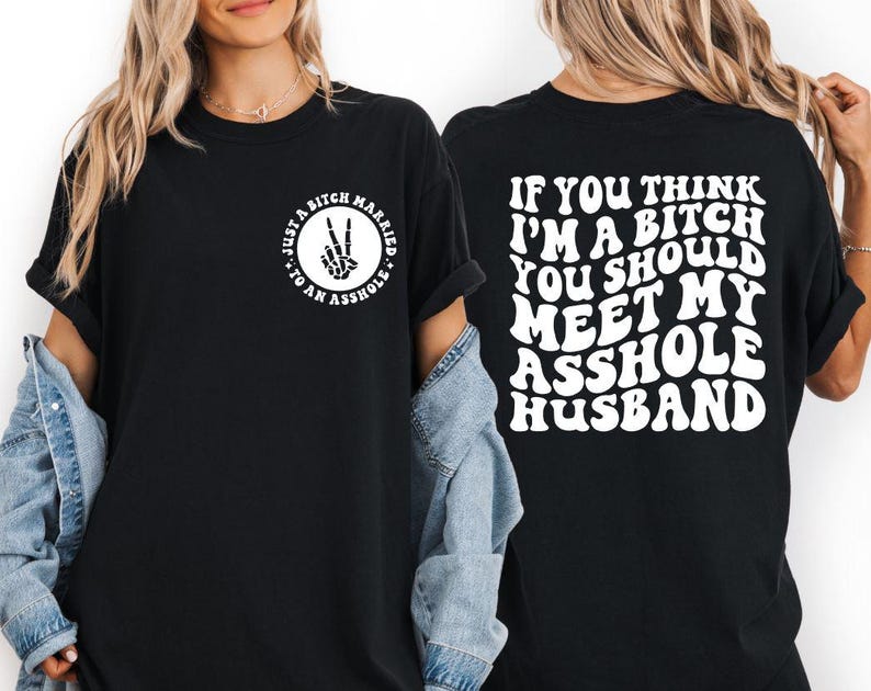 May include: Black t-shirt with white text on the front and back. The front features a circle with a peace sign made of bones and the words "Just a Bitch Married to an Asshole." The back says, "If you think I'm a bitch you should meet my asshole husband."