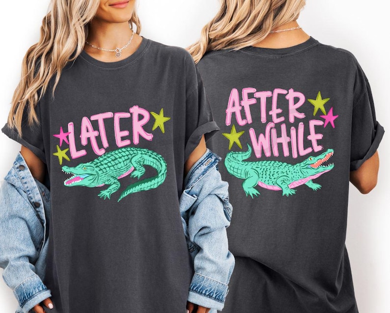 May include: Dark gray t-shirt with a teal alligator graphic and the word "LATER" in pink letters with yellow and pink stars. The back of the shirt says "AFTER WHILE" with the same alligator graphic.