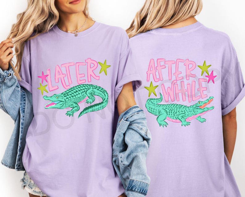 May include: A light purple t-shirt featuring a green alligator graphic with the text "LATER" on the front and "AFTER WHILE" on the back. The design includes pink and yellow stars. The shirt has short sleeves.