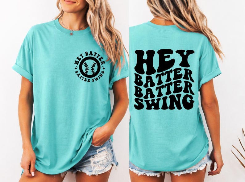 K&ouml;nnte beinhalten: T&uuml;rkisfarbenes T-Shirt mit dem schwarzen Text "HEY BATTER BATTER SWING". Auf der Vorderseite des Shirts befindet sich eine Baseball-Grafik mit demselben Text. Das Shirt hat einen l&auml;ssigen, bequemen Stil.
