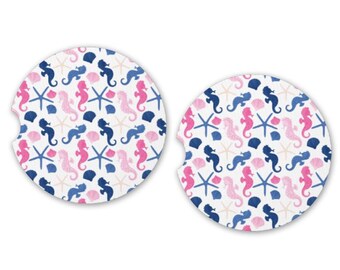 Può includere: Due sottobicchieri rotondi bianchi con un motivo ripetuto di cavallucci marini rosa e blu, conchiglie e stelle marine.