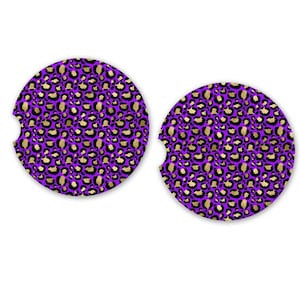 May include: Two round car coasters with a purple background and a gold and black leopard print pattern. Each coaster has a small semi-circular cutout on one side.