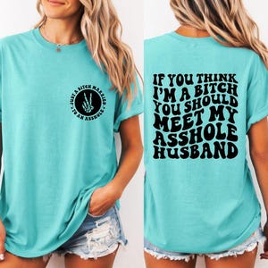 May include: Turquoise t-shirt with the text "Just a bitch married to an asshole" and a skeleton hand peace sign. The back of the shirt has the text "If you think I'm a bitch you should meet my asshole husband."