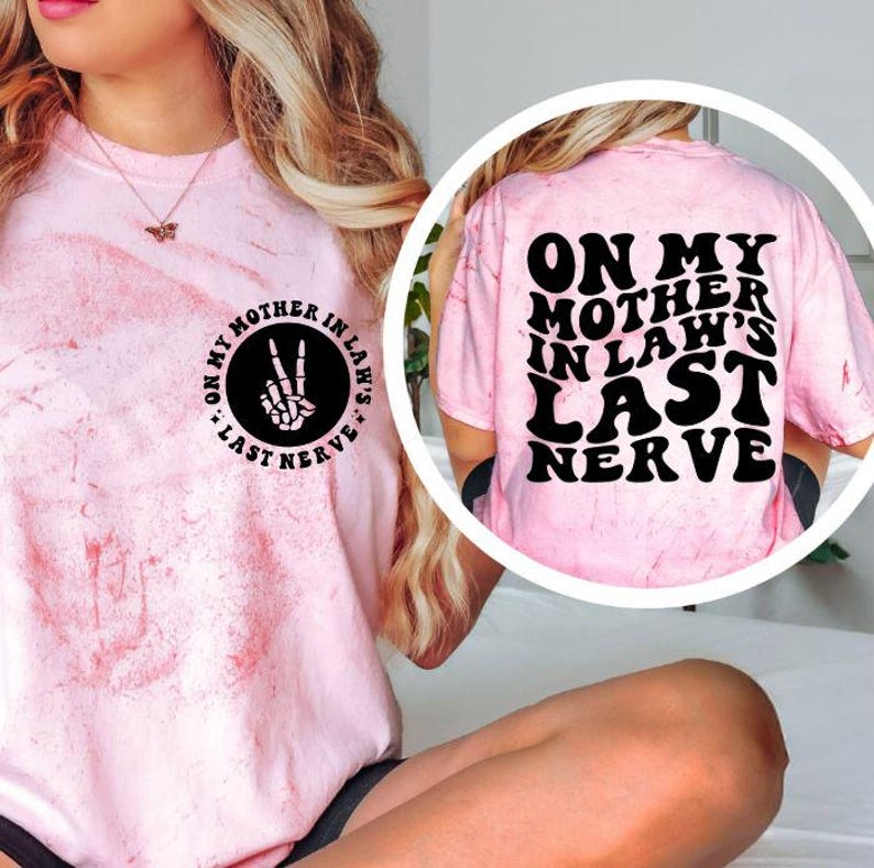 May include: Pink tie-dye t-shirt with the text "ON MY MOTHER IN LAW'S LAST NERVE" in black. The front of the shirt has a circular graphic with the text "ON MY MOTHER IN LAW'S" and a peace sign made of bones.