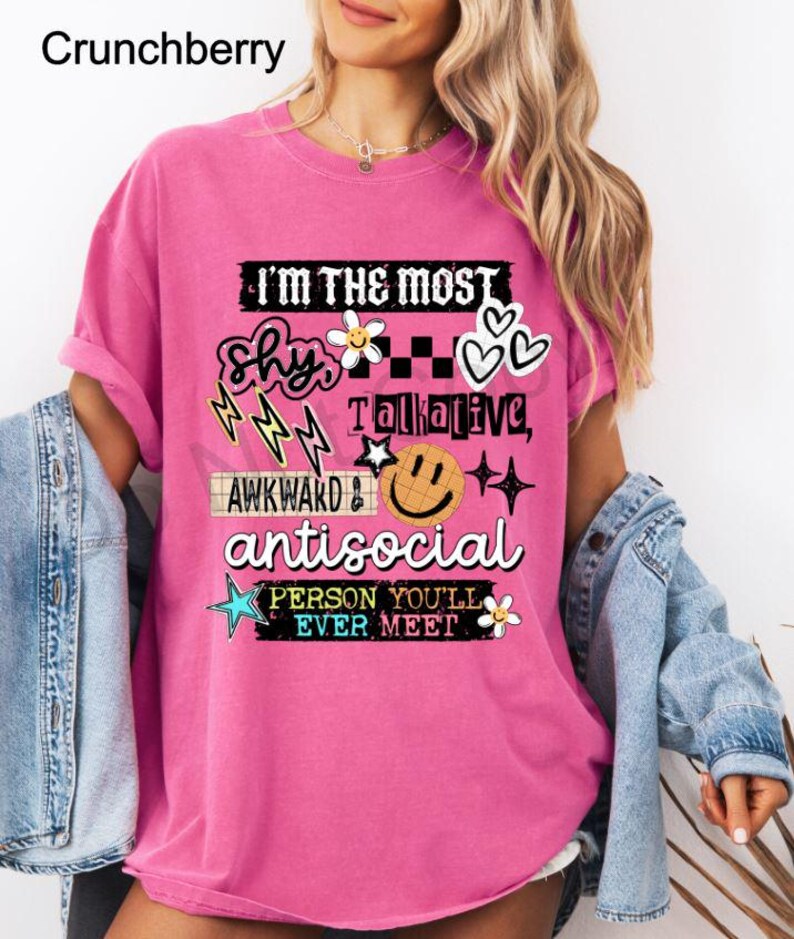 K&ouml;nnte beinhalten: Ein pinkfarbenes T-Shirt mit dem Text "I'M THE MOST shy, awkward, antisocial PERSON YOU'LL EVER MEET." Das Design umfasst Blitze, Blumen, Herzen, Sterne und ein Smiley. Das Shirt ist einfarbig.