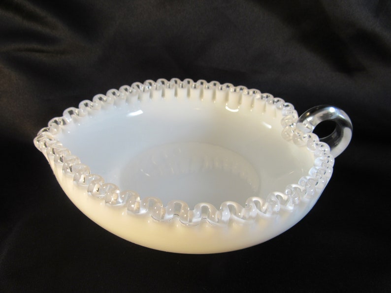 May include: A white milk glass bowl with a scalloped edge and a clear glass handle. The bowl has a silver-colored trim around the edge.