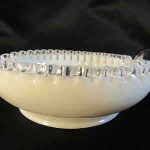 May include: White milk glass bowl with a silver rim and two handles. The bowl has a scalloped edge.