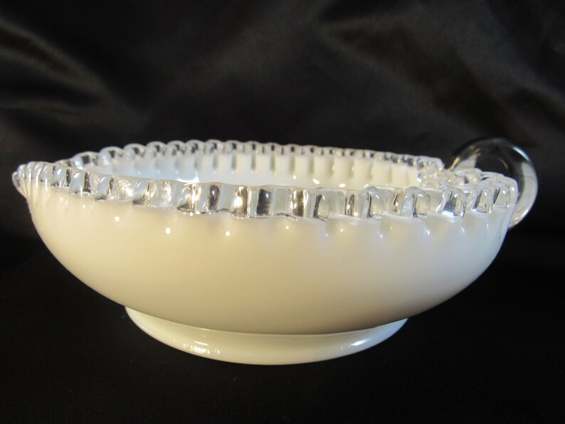 May include: White milk glass bowl with a silver rim and two handles. The bowl has a scalloped edge.