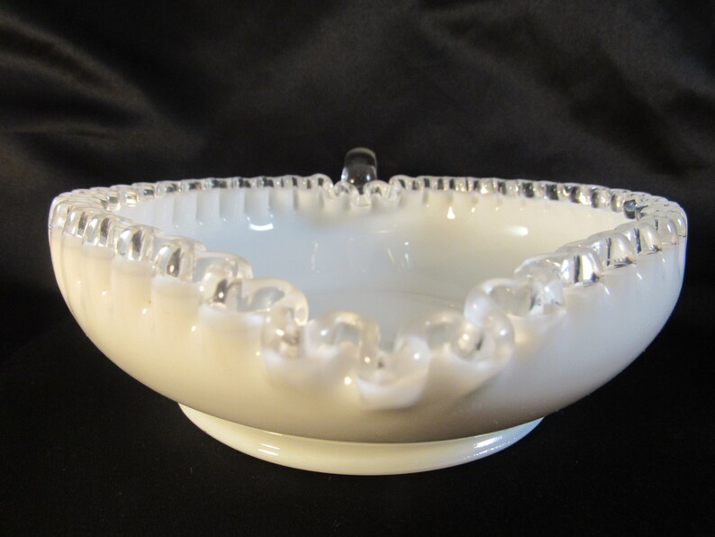May include: White milk glass bowl with a silver trim and a ruffled edge. The bowl has a small handle on the top.