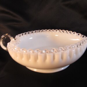 May include: A white milk glass creamer with a silver beaded edge and a handle. The creamer has a fluted design and a small base.