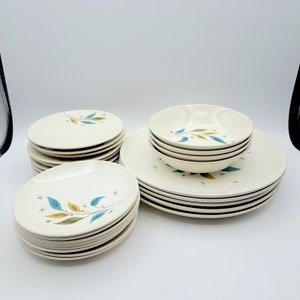 May include: A set of vintage white ceramic dinnerware with a blue and yellow leaf design. The set includes plates and bowls.