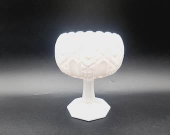 May include: A white milk glass candy dish with a pedestal base. The dish has a diamond pattern and a raised rim.