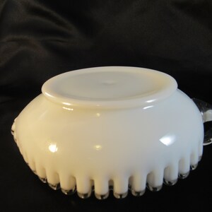 May include: White milk glass bowl with a scalloped edge and a clear glass handle. The bowl has a smooth, glossy finish.