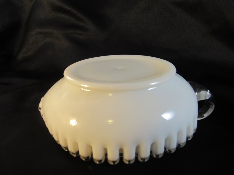 May include: White milk glass bowl with a scalloped edge and a clear glass handle. The bowl has a smooth, glossy finish.