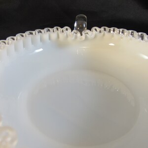 May include: White milk glass bowl with a silver rim and a clear glass handle. The bowl has a scalloped edge and a smooth, white interior.